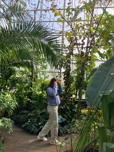 a woman taking a photo in a greenhouse with her cell phone while walking through the plants