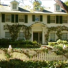 a large white house with ivy growing on it's walls and bushes around the front yard