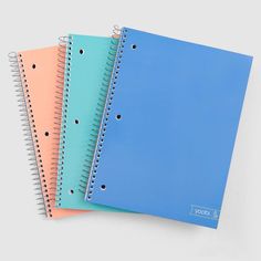 three spiral bound notebooks sitting next to each other on top of a pink surface