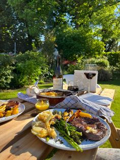 two plates of food on a picnic table with glasses of wine and bottles of wine in the background