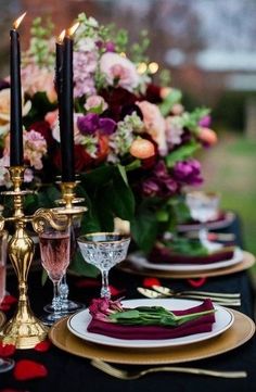 the table is set with black and red place settings, gold candlesticks, and pink flowers