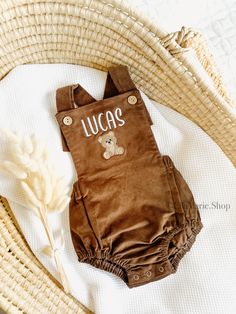 a brown teddy bear romper with the word lucas written on it, sitting next to a wicker basket