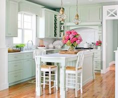 a kitchen with green cabinets and white counter tops, two stools at the island