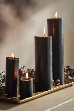 three lit candles sitting on top of a tray next to some flowers and greenery