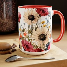 a red and white coffee mug sitting on top of a wooden table next to a spoon