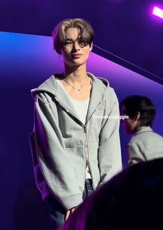 a man standing in front of a purple background wearing a gray hoodie and jeans