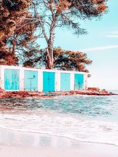 an old building sitting on the beach next to the ocean with blue doors and windows