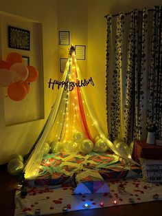 a birthday cake with balloons and lights on the table in front of a curtained window