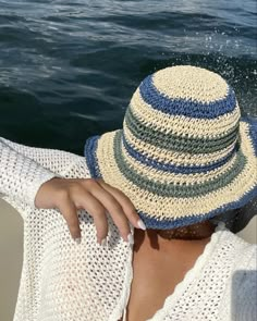 a woman wearing a hat sitting on top of a boat near the water with her hands behind her head