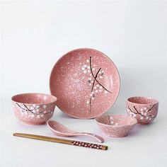 a set of pink dishes and spoons on a white surface with cherry blossoms painted on them