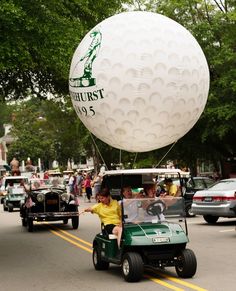 a golf cart driving down the street with people in it and a large white ball on top