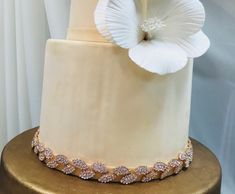 a three tiered wedding cake with white flowers on the top and gold trimmings