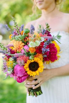 a woman in a white dress holding a bouquet of sunflowers and other flowers