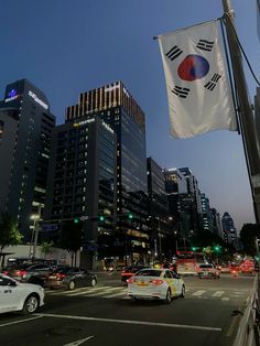 cars are driving down the street in front of tall buildings at night, with a flag flying above them