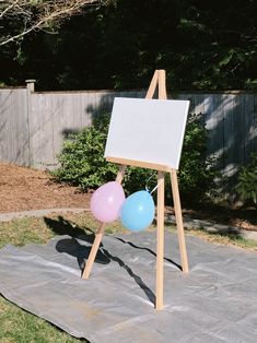 an easel with balloons in front of it and a white board on the ground