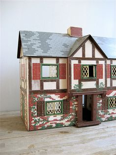 a doll house with red shutters and green trim on the windows, door and porch