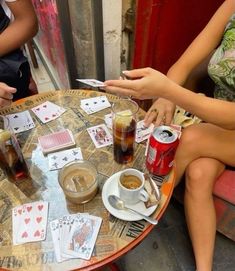 two people sitting at a table with playing cards and cups of coffee on the table