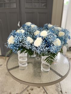 blue and white flowers are arranged in vases on a glass table with a door behind them