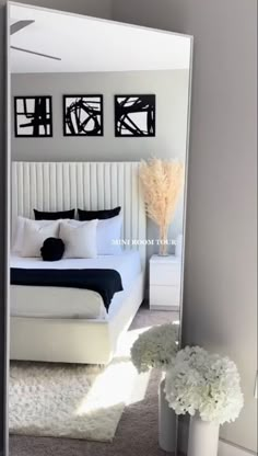 a white bed sitting under a mirror next to a vase with flowers on top of it