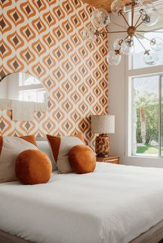 a large bed sitting under a window next to a wall mounted mirror and lamp on top of it