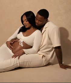 a man and woman are sitting on the floor together, one is holding her belly