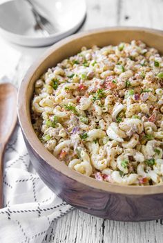 a wooden bowl filled with macaroni salad on top of a white tablecloth