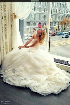 a woman in a wedding dress is sitting on the window sill looking out at the street