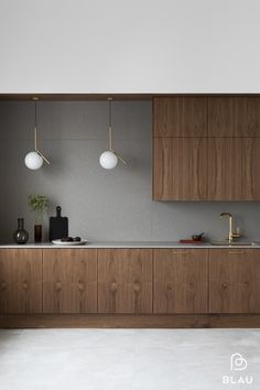 a modern kitchen with wood cabinets and white counter tops is pictured in this image, there are two pendant lights above the sink