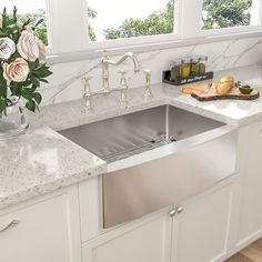 a white kitchen with marble counter tops and stainless steel double basin sinks, along with flowers