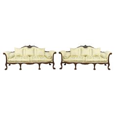 a pair of victorian style sofas with white upholstered cushions and carved wood feet