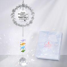 a white box with a silver necklace hanging from it's side next to a glass bead wind chime