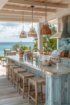 an outdoor kitchen with blue cabinets and white counter tops, hanging lights over the island