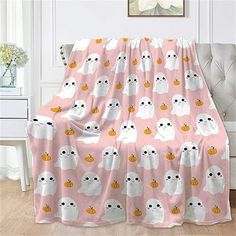 a pink blanket with ghost faces and pumpkins on it in front of a chair