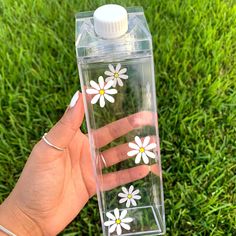 a hand holding a clear water bottle with white flowers painted on the front and sides