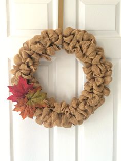 a burlock wreath hanging on a door with fall leaves in front of it