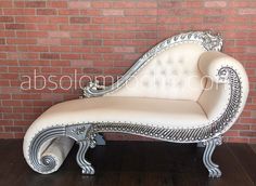 an ornate white chaise lounge chair in front of a brick wall and hardwood floor