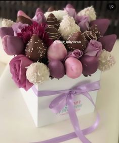 a white box filled with chocolates and flowers on top of a table next to a purple ribbon