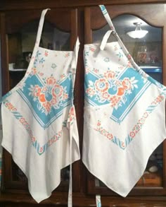 two aprons are hanging on the back of a wooden hutch, both with blue and orange designs