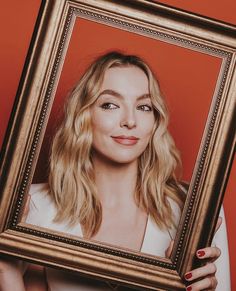 a woman holding up a framed photo with her face in the frame and red background