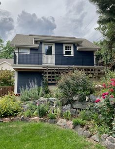 a house that is in the middle of some grass and flowers on the side of it