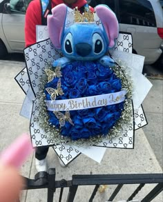 a person holding a bouquet of blue roses in front of a disney character birthday cake