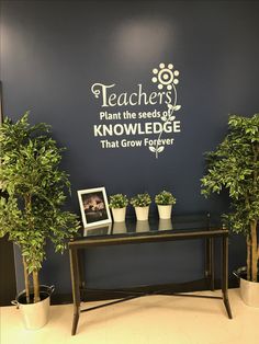 two potted plants sit on a table in front of a wall with the words teachers plant the seeds of knowledge that grow forever