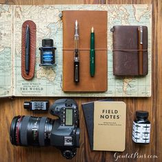 the contents of a travel bag laid out on top of a map with a camera, notebook and pen