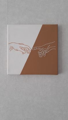 two hands touching each other over a brown and white painting on a gray wall with one hand holding the other's hand