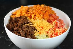 a white bowl filled with meat, cheese and veggies on top of a black table