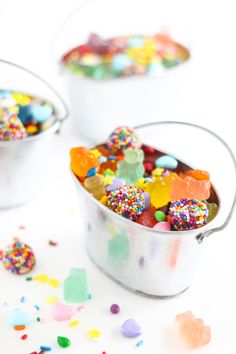 two buckets filled with different colored candies and sprinkles on a white surface