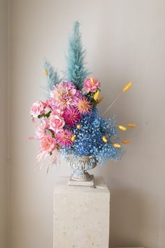 a vase filled with lots of colorful flowers on top of a white table next to a wall