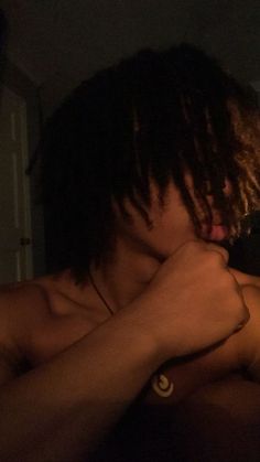 a shirtless man with dreadlocks is looking at his cell phone in the dark