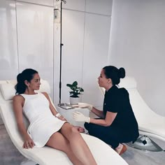 two women in white dresses sitting at a table and one is getting her nails done