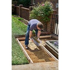 a man is shoveling dirt into a raised garden bed in front of a brick house